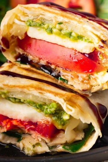 Caprese tuna melt wrap with tomato, mozzarella, pesto, and sauce, served on a black plate with greens in the background.