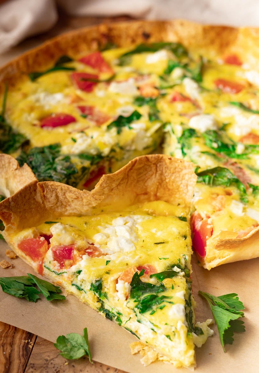 Egg tortilla bake with spinach, tomatoes, and cheese on parchment paper.