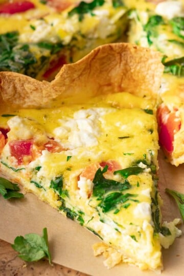 Egg tortilla bake with spinach, tomato, and cheese on a wooden surface with parsley garnish.