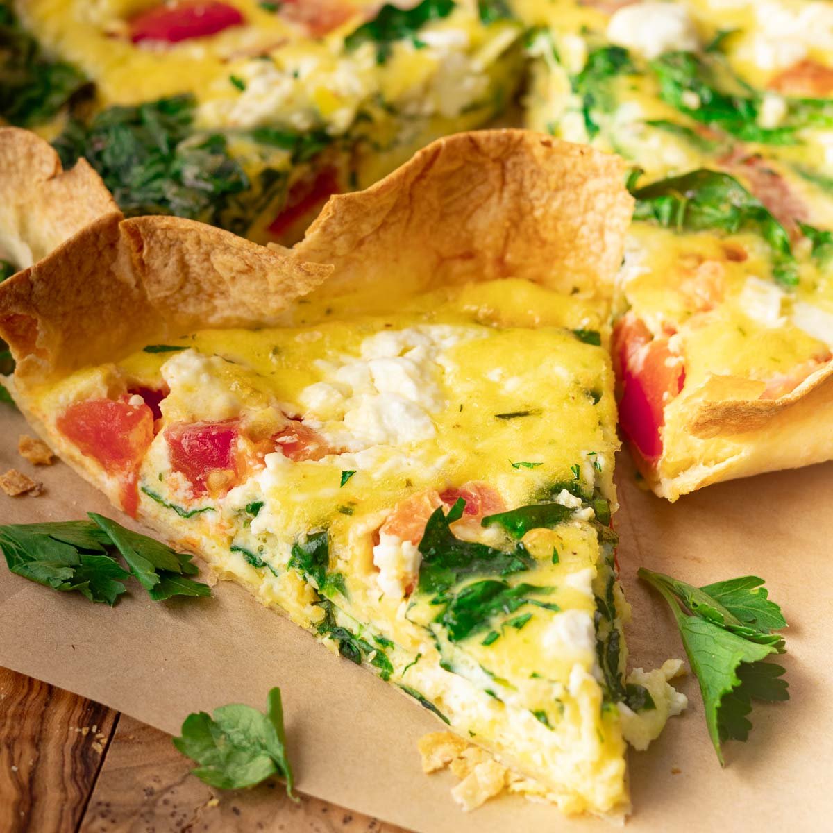 Egg tortilla bake with spinach, tomato, and cheese on a wooden surface with parsley garnish.