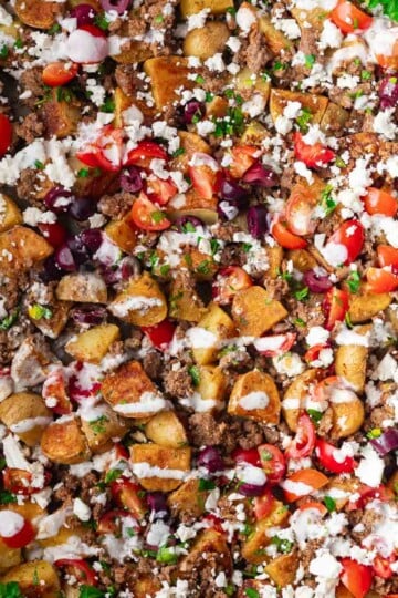Sheet pan roasted potatoes, ground beef, cherry tomatoes, olives, feta cheese, creamy sauce, herbs.
