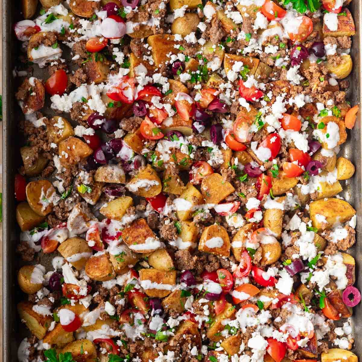 Sheet pan roasted potatoes, ground beef, cherry tomatoes, olives, feta cheese, creamy sauce, herbs.