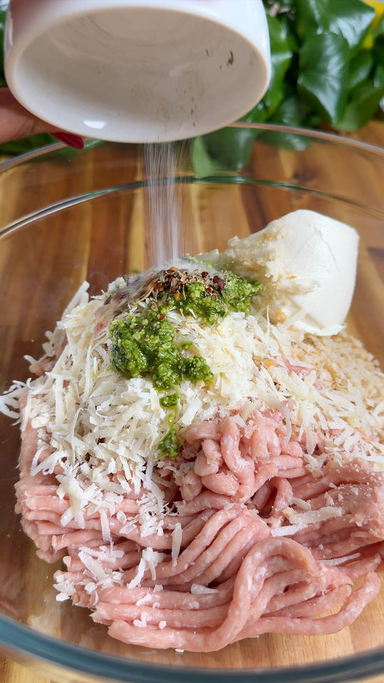 Ground chicken with cheese, pesto, and breadcrumbs in a bowl being seasoned.