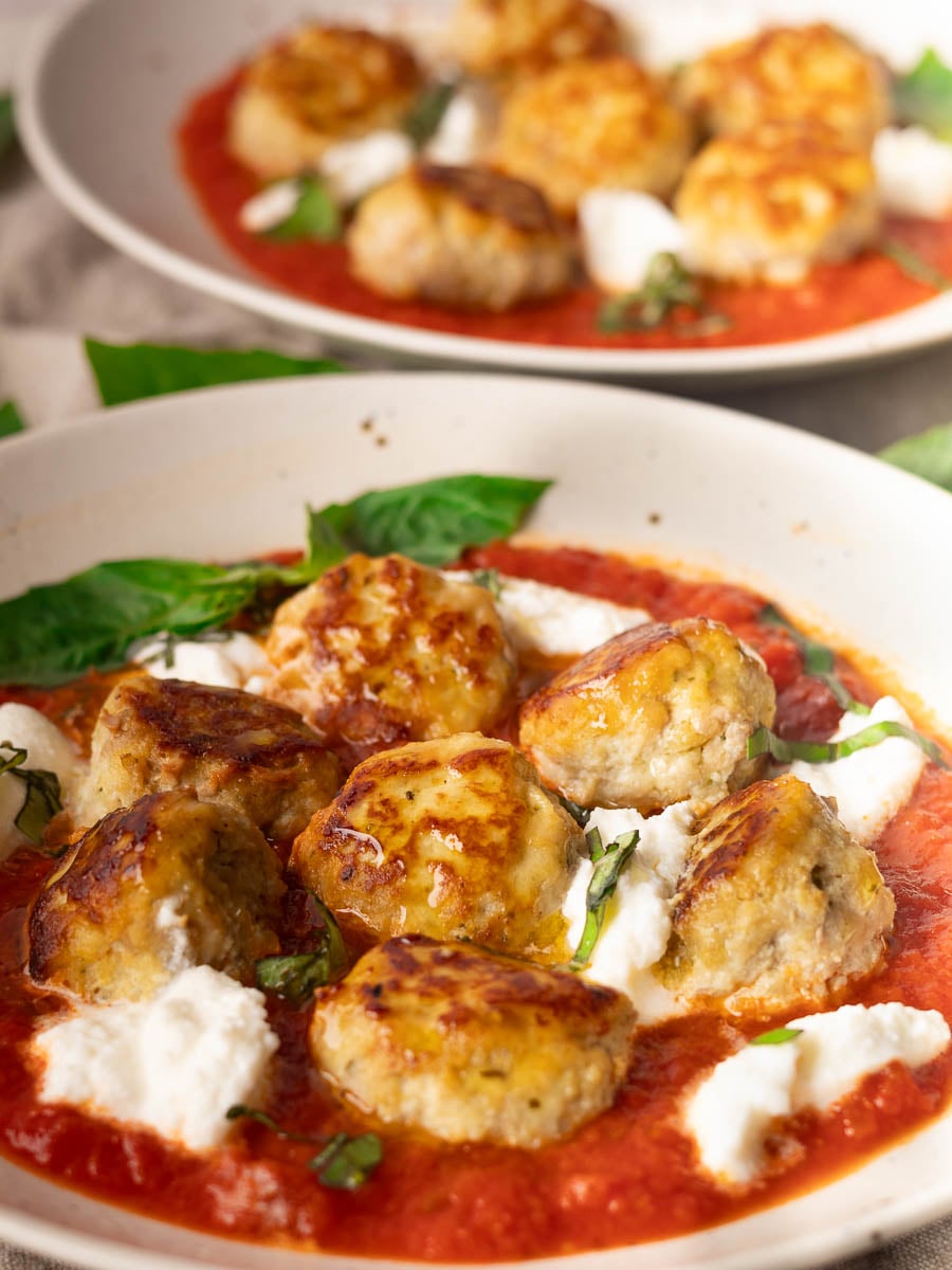 Ricotta meatballs in tomato sauce with fresh basil and ricotta cheese served on a plate.