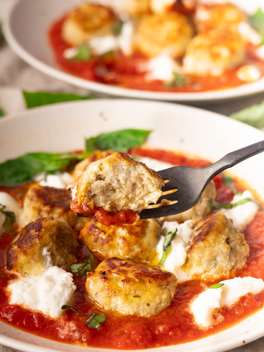 Ricotta meatballs with tomato sauce, fresh basil, and ricotta on a plate, fork holding a meatball piece.