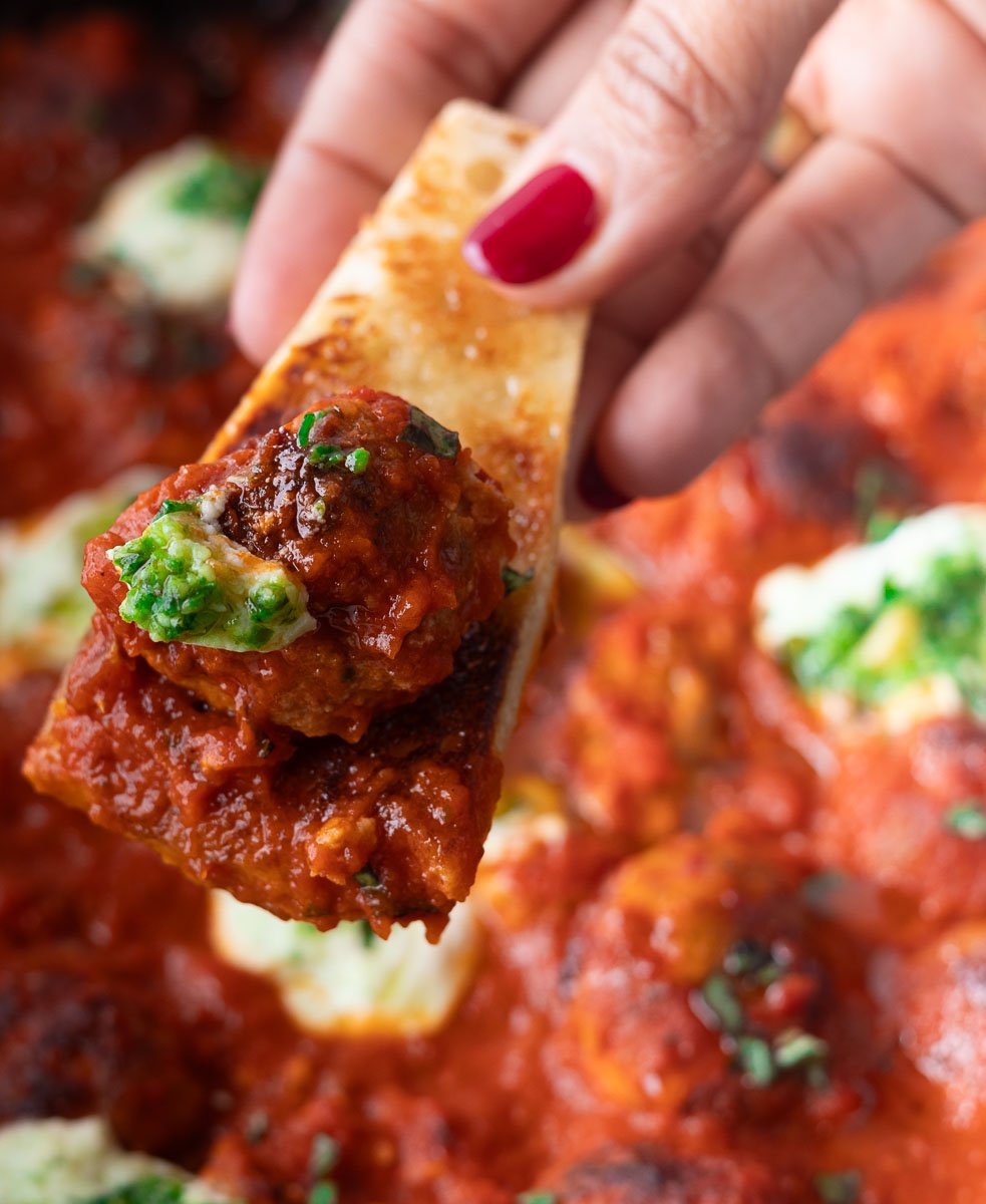 Hand holding bread topped with Ricotta meatballs, cheese, and herbs.