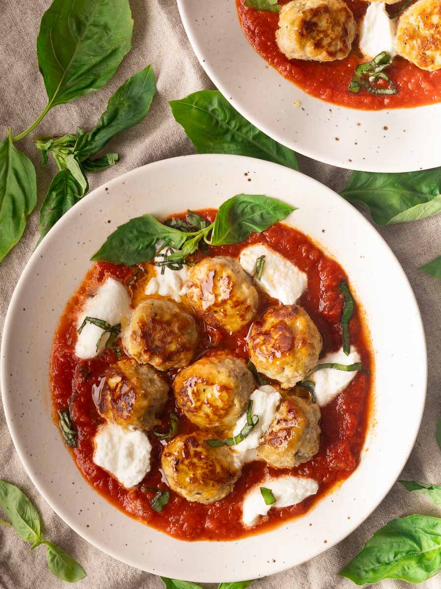 Ricotta meatballs in tomato sauce with mozzarella, garnished with fresh basil on a white plate.
