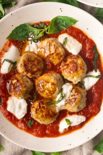Ricotta meatballs in tomato sauce with mozzarella and basil garnish.