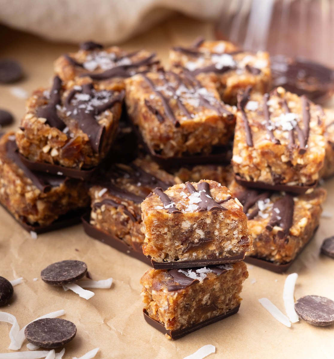 Samoas cookie bites stacked on parchment paper with coconut flakes and chocolate chips.