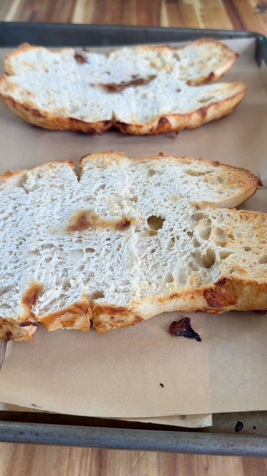 Toasted focaccia bread slices on a baking tray with parchment paper.