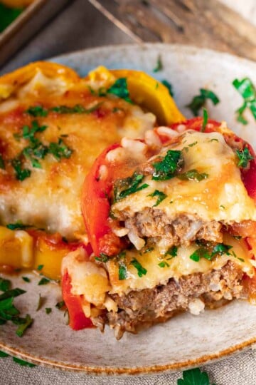 Baked stuffed bell peppers with cheese and herbs on a white plate, showcasing a cut section filled with minced meat.