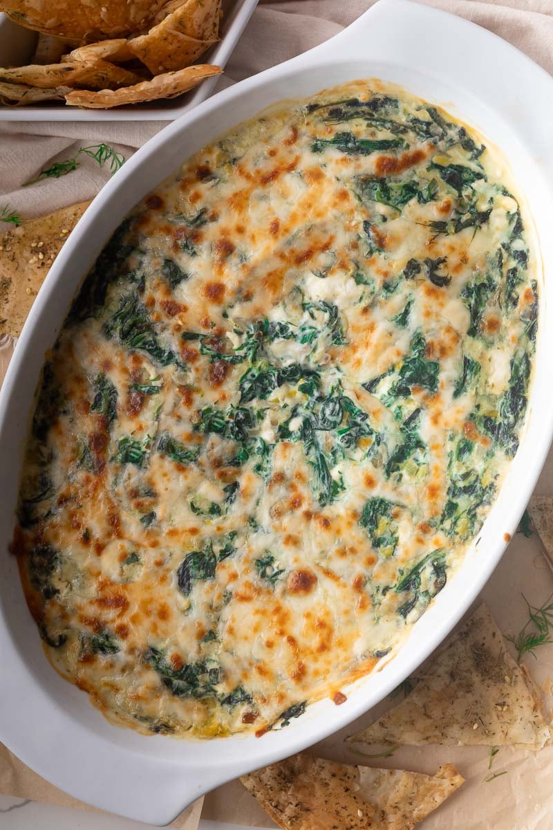 spanakopita dip in white dish with pita chips on side.
