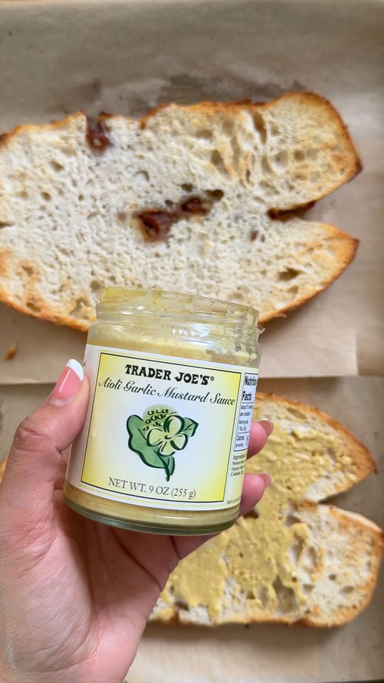 Jar of Trader Joe's Aioli Garlic Mustard Sauce held over slices of bread on parchment paper.