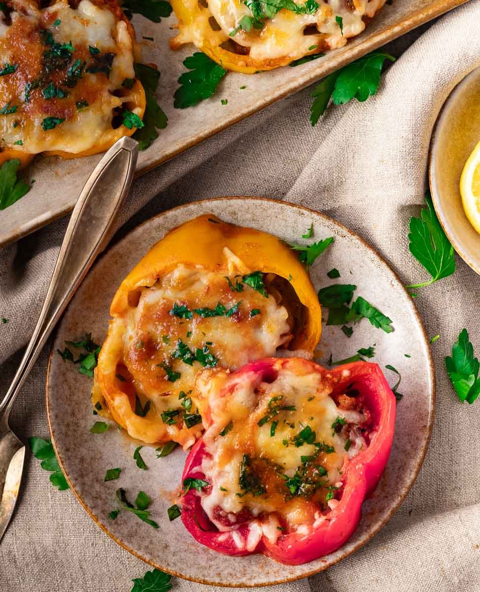 Stuffed bell peppers topped with melted cheese and parsley on a ceramic plate with cutlery and a napkin.