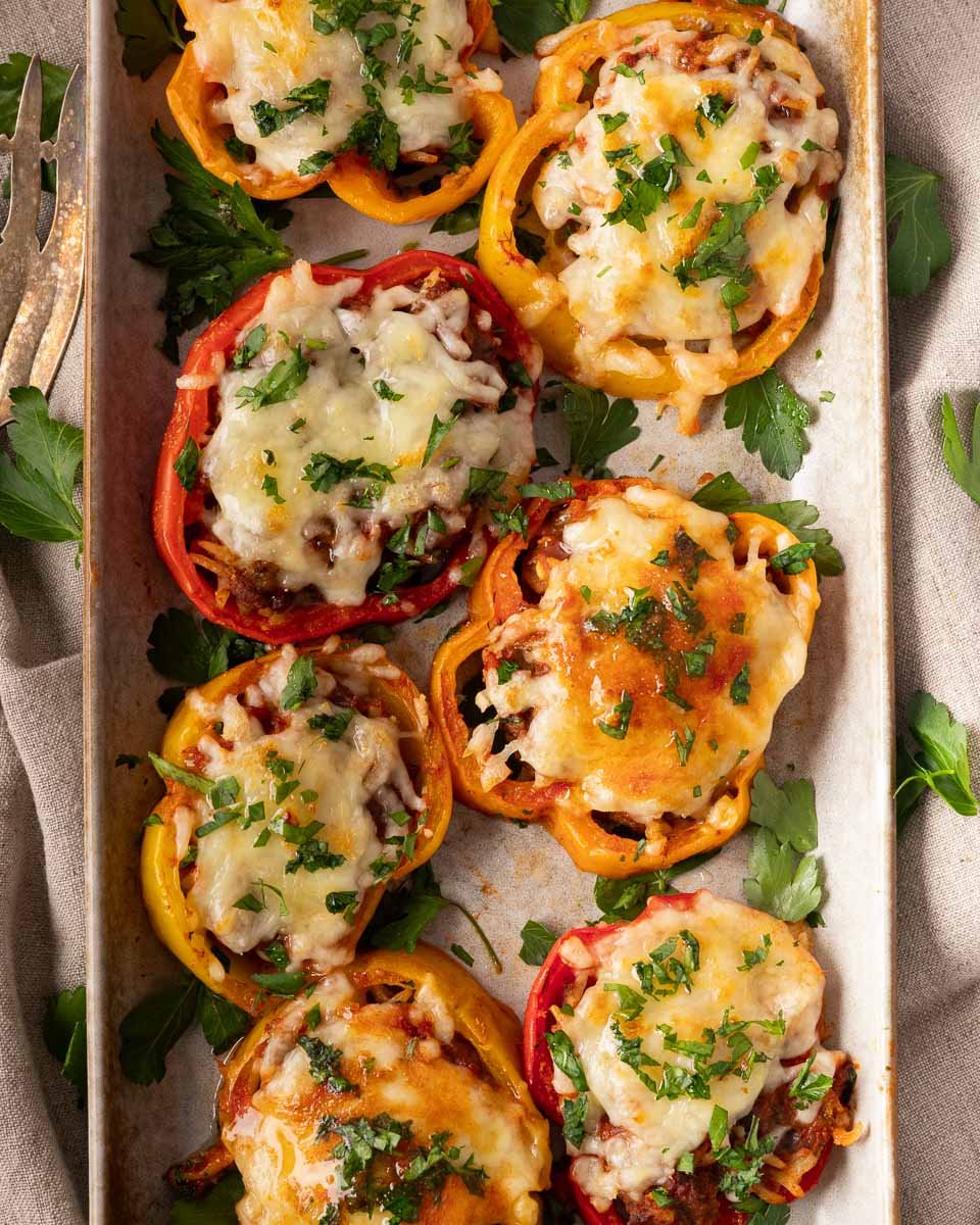 Stuffed bell pepper rings with melted cheese and parsley garnish on a baking sheet.