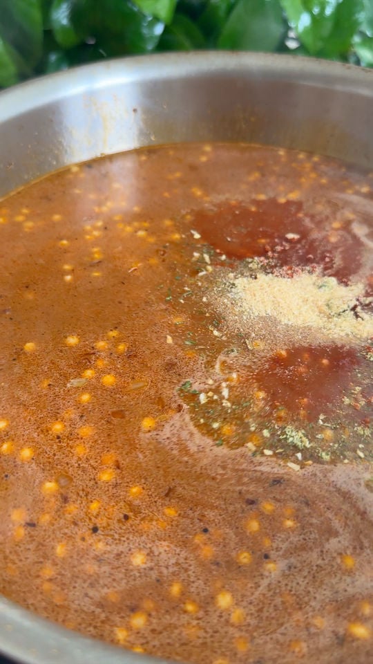 Broth in a pot with visible spices and herbs on the surface.