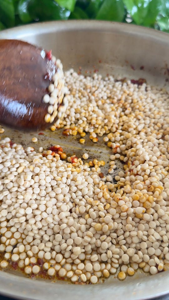 Toasting couscous with a wooden spoon in a pan.