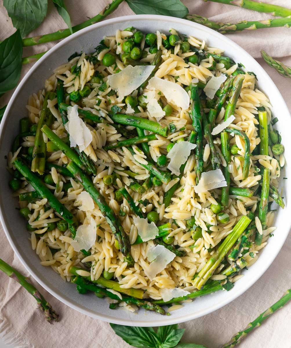 Asparagus-orzo pasta salad with asparagus, peas, and Parmesan in a bowl, garnished with fresh basil leaves.