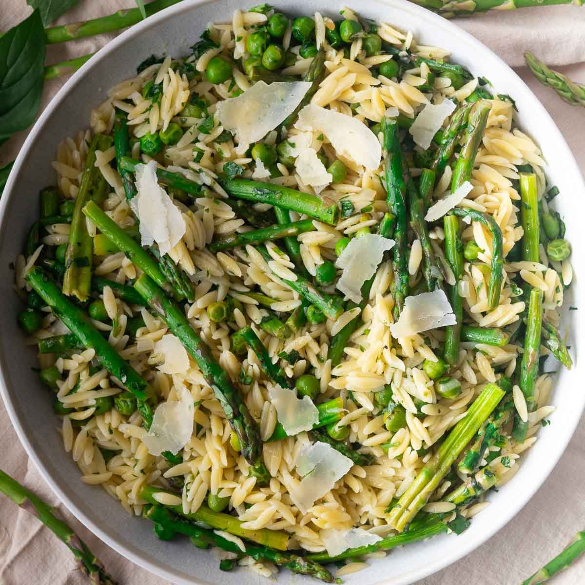 Asparagus Orzo Pasta Salad with asparagus, peas, and parmesan in a white bowl.