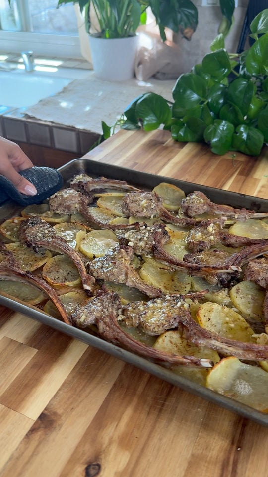 Baked lamb chops with sliced potatoes and garlic on a tray.