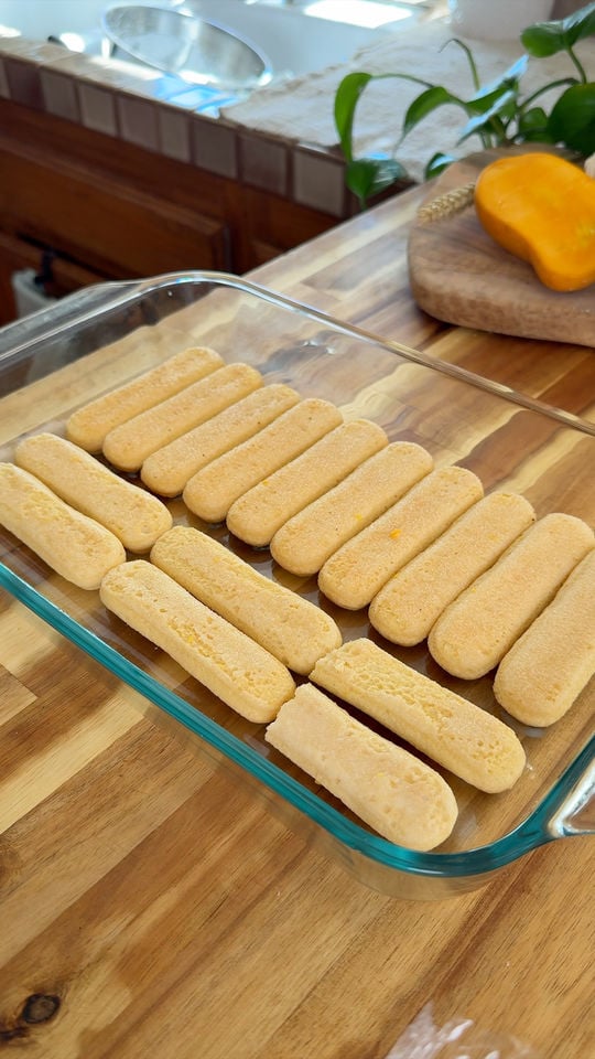 Ladyfinger biscuits arranged in a glass baking dish on a wooden countertop.