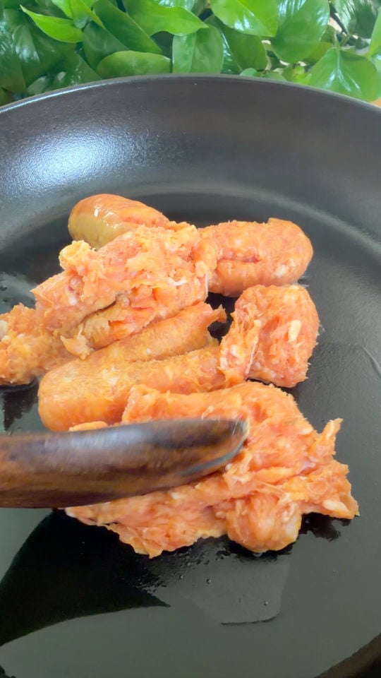 Cooking crumbled sausage in a black frying pan.