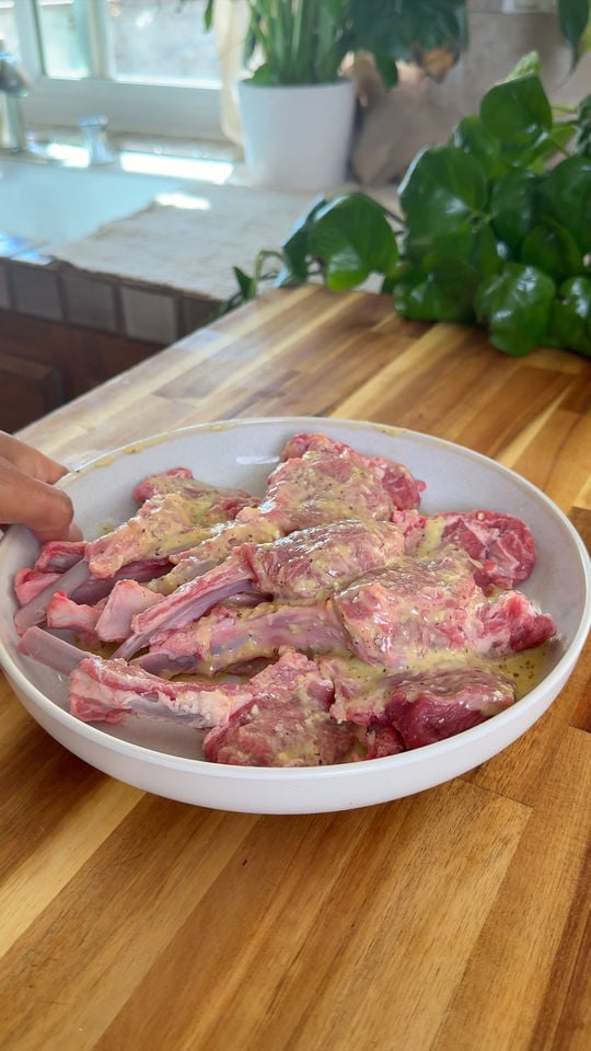 Raw lamb chops marinated in a sauce on a white plate.