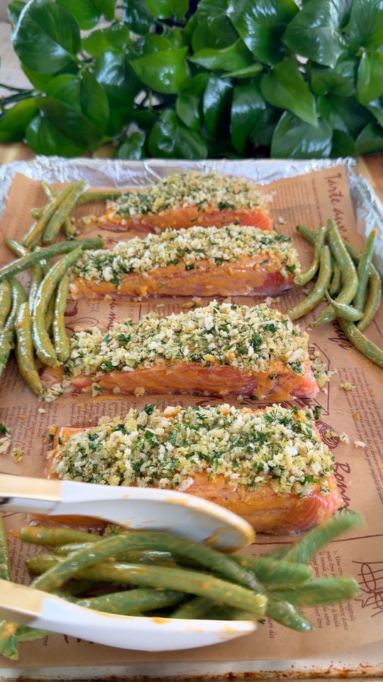 Baked salmon filets with herb crust and green beans on a baking tray.