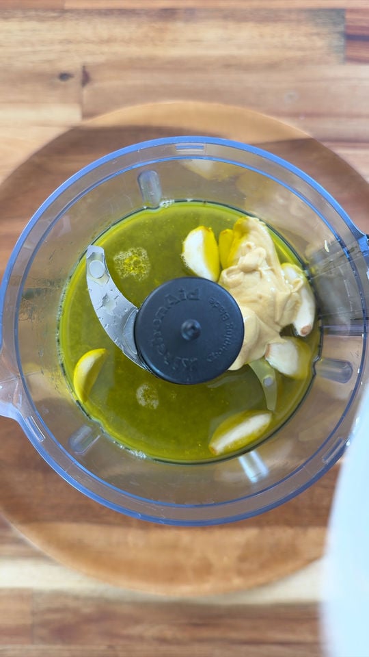 Food processor with olive oil, garlic on a wooden surface.