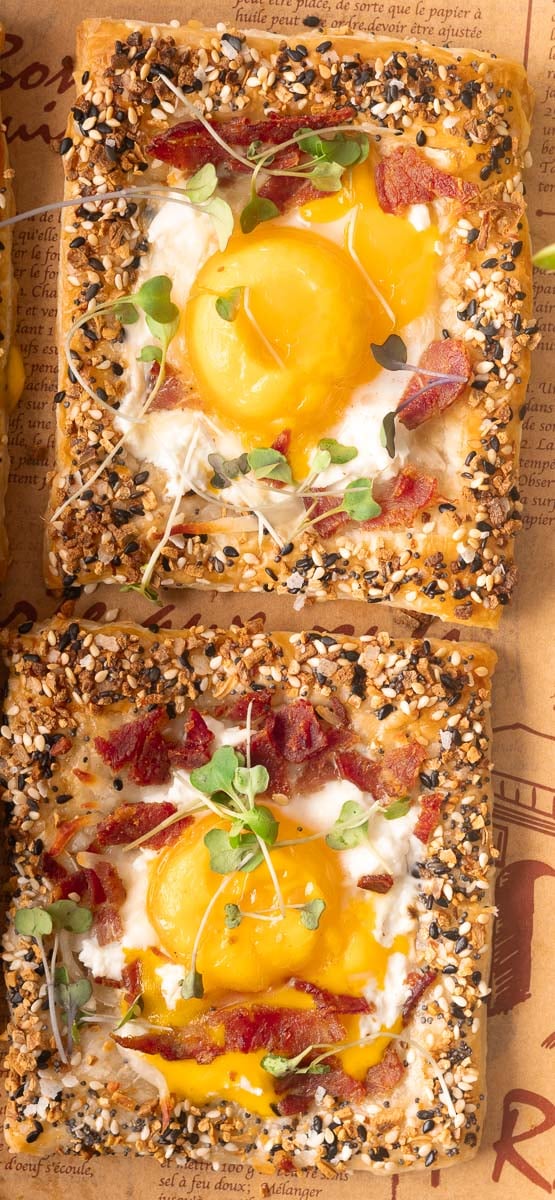 Two puff pastry breakfast pizza with eggs, bacon, and microgreens on a rustic background.