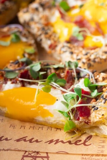 Close-up of a puff pastry breakfast pizza sesame seeds, melted cheese, runny egg yolk, and microgreens on a parchment paper.