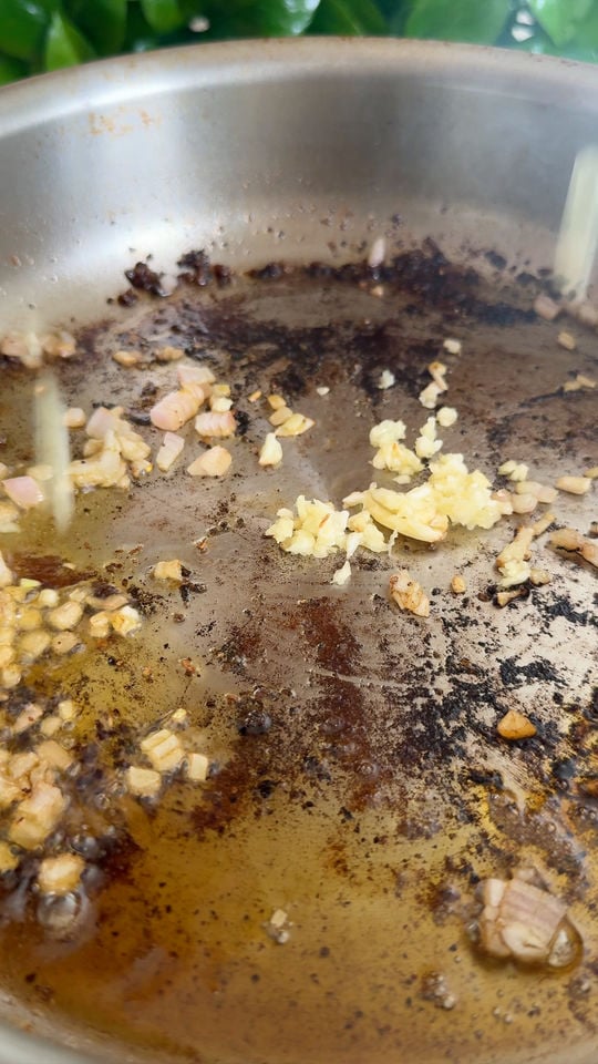 Garlic and shallots sautéing in oil in a stainless steel pan.
