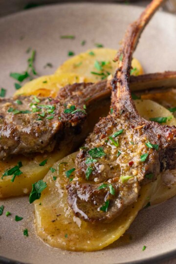 Sheet pan baked lamb chops on sliced potatoes, garnished with fresh parsley on a plate.