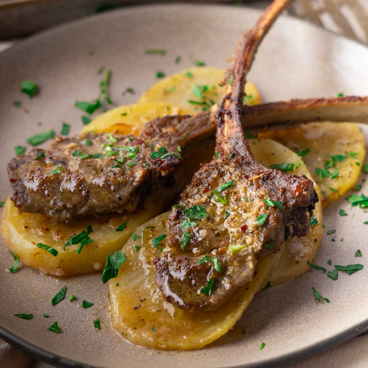 Sheet pan baked lamb chops on sliced potatoes, garnished with fresh parsley on a plate.
