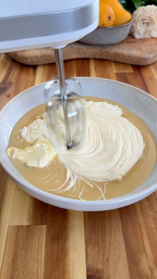 Mixer blending creamy ingredients in a bowl on a wooden table.