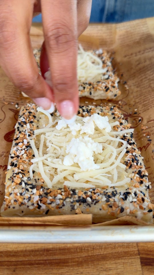 Hand sprinkling cheese on sesame seed crusted pastry on parchment.