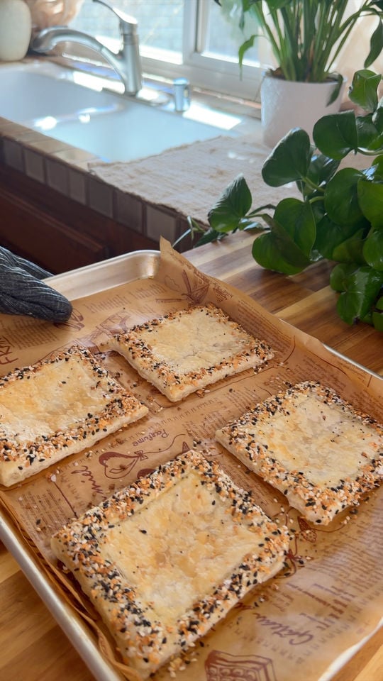 Baked pastry squares with sesame seed edges on a paper-lined tray.