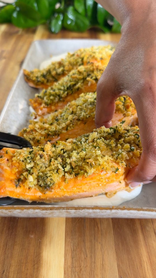 Hand serving crusted salmon fillet on a bed of yorgurt.