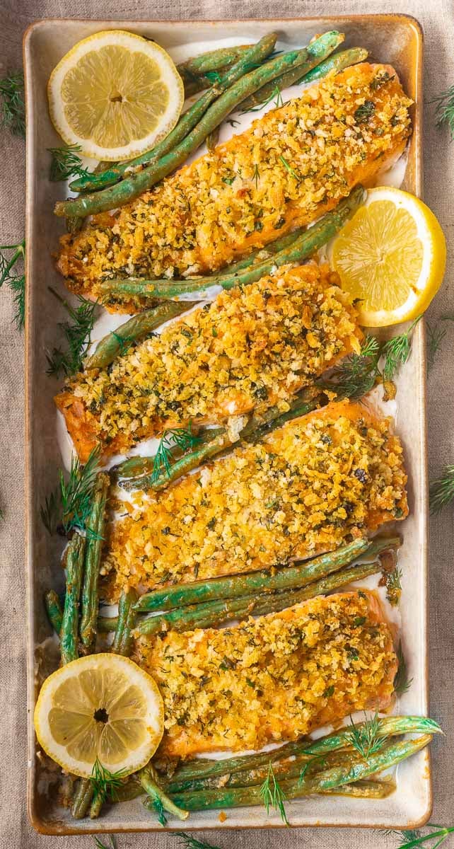 Baked panko crusted salmon with breadcrumb topping, surrounded by green beans and lemon slices on a rectangular platter.