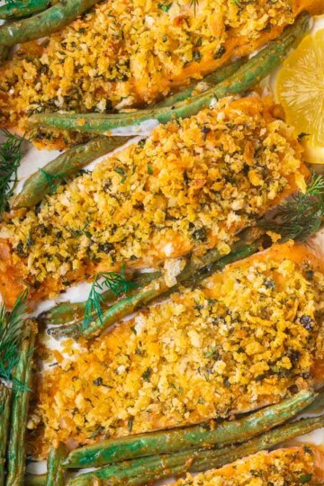 Baked panko crusted salmon with mayo topped with herb crust, surrounded by green beans and garnished with fresh dill and lemon slice.
