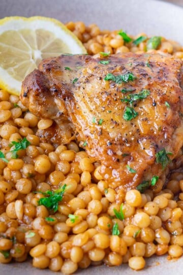 Roasted chicken thigh on a bed of spiced pearled couscous with parsley and lemon slice garnish.