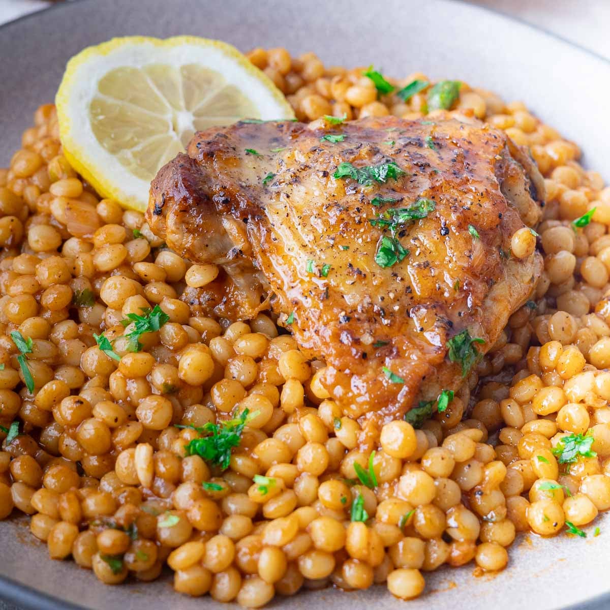 Roasted chicken thigh on a bed of spiced pearled couscous with parsley and lemon slice garnish.