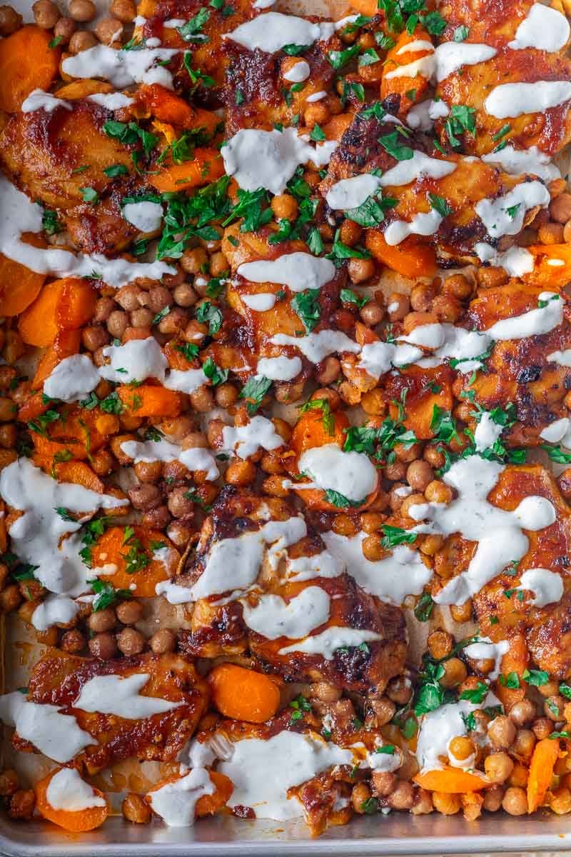 Honey harissa chicken tray bake with roasted chicken thighs with carrots and chickpeas, drizzled with creamy sauce and garnished with chopped parsley.