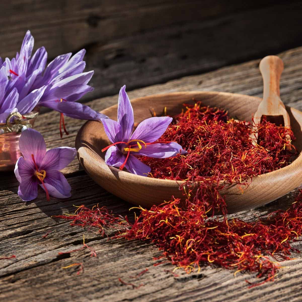 Purple crocus flowers and saffron threads in a wooden bowl on a rustic wooden surface.