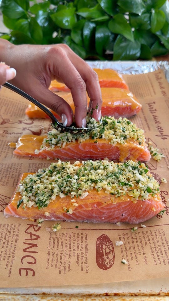 Hand preparing herb-crusted salmon fillets on parchment paper.