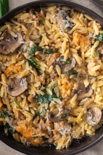 Chicken sausage and mushroom orzo in a black bowl, garnished with fresh basil leaves.