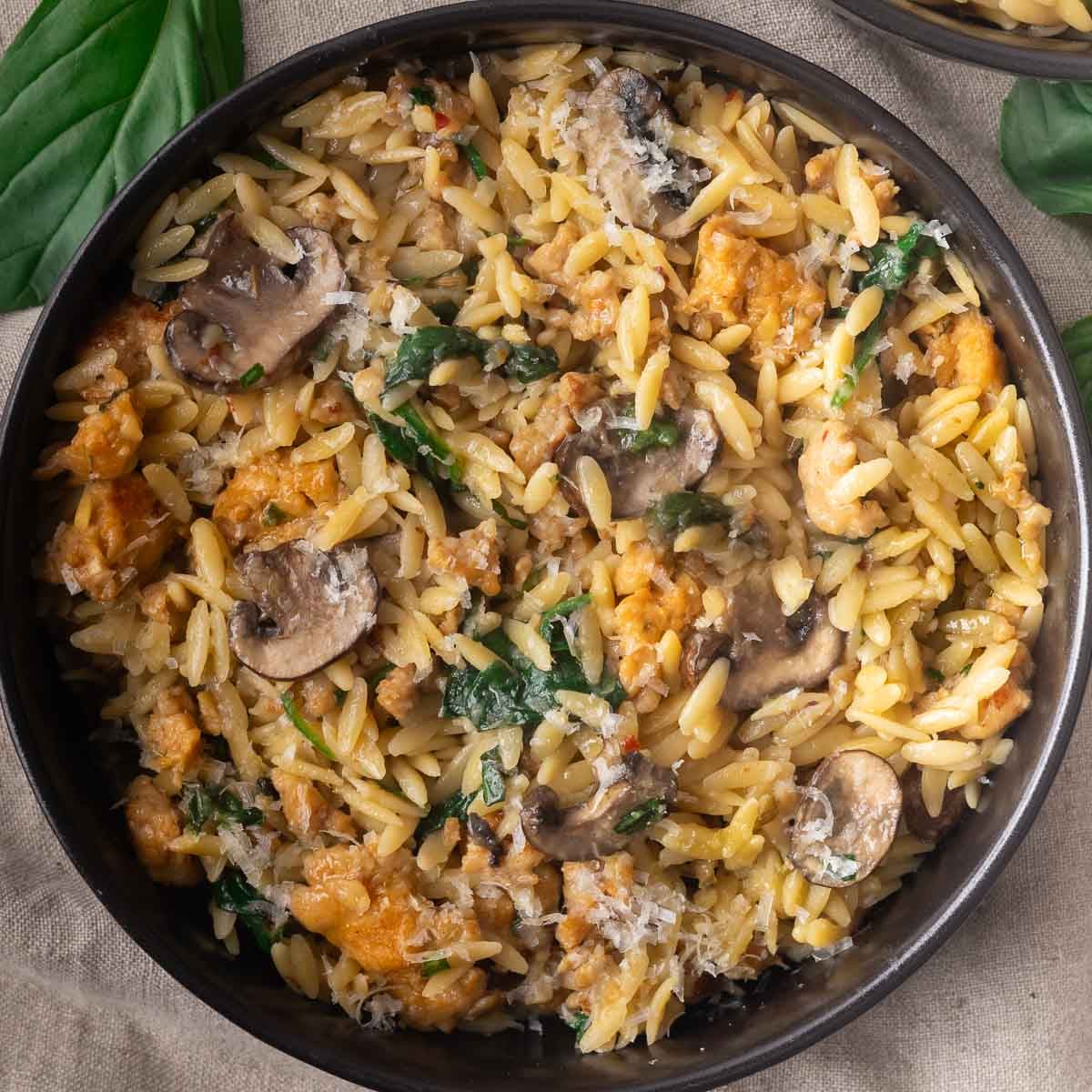 Chicken sausage and mushroom orzo in a black bowl, garnished with fresh basil leaves.