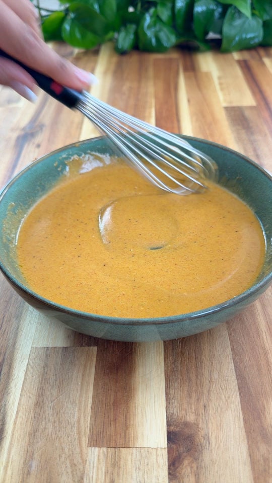 Whisking sauce in a green bowl on a wooden table.