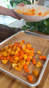 Carrots and potatoes on a lined baking sheet with sauce.