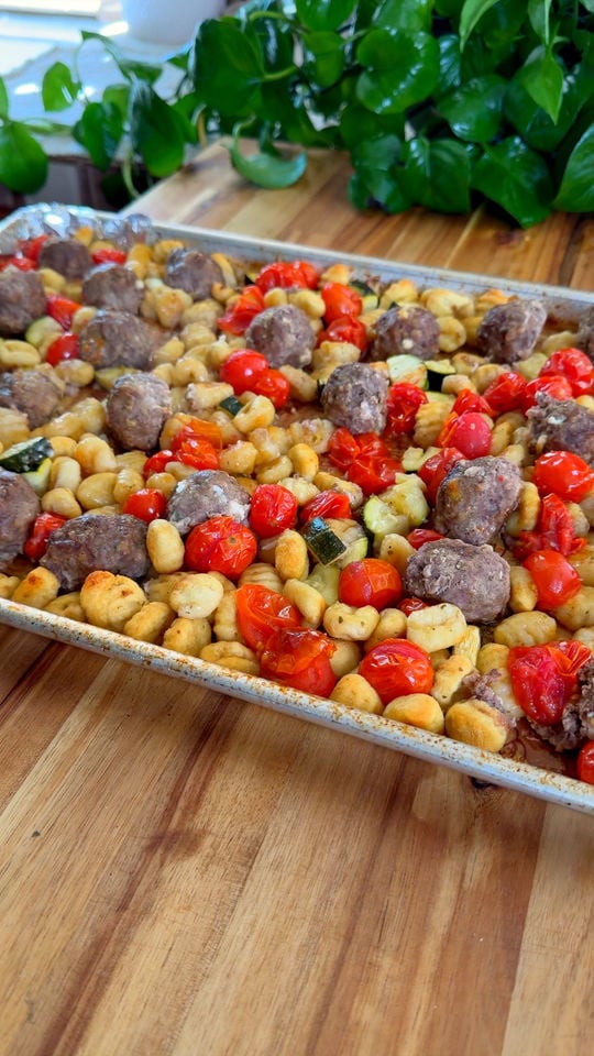 Roasted meatballs, cherry tomatoes, zucchini, and gnocchi on a baking tray.
